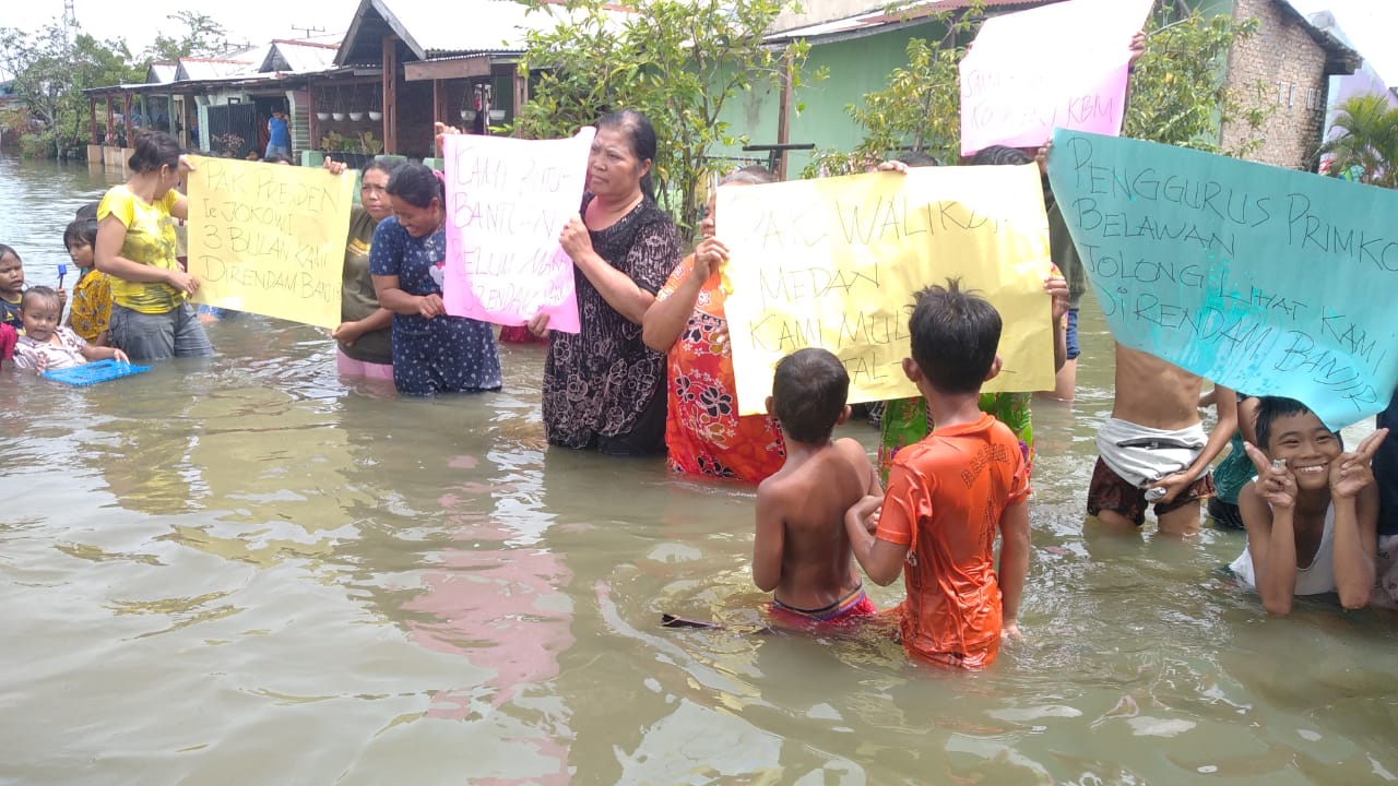KAUM ibu dan anak-anak memperlihatkan sejumlah poster saat melakukan aksi unjuk rasa di tengah-tengah genangan banjir yang melanda Komplek Perumahan Buruh TKBM Upaya Karya Pelabuhan Belawan, Kelurahan Sei Mati, Kecamatan Medan Belawan, Senin (21/11). Waspada/Ist