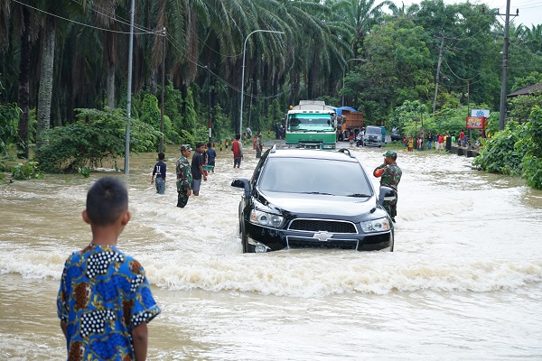 Personel Koramil Kejuruan Muda jajaran Kodim 0117/ Aceh Tamiang terjun langsung mengatur arus lalulintas pada ruas jalan negara yang tergenang air banjir di Kebun Tengah, Kec Kejuruan Muda, Aceh Tamiang. (Waspada.id/ Yusri).