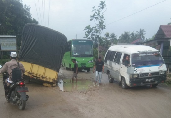 Jalan lintas provinsi Sumut di desa Sakkilon rusak dan berlubang membuat truk sarat muatan terperosok dan terjebak. (Waspada/H. Idaham Butar Butar)