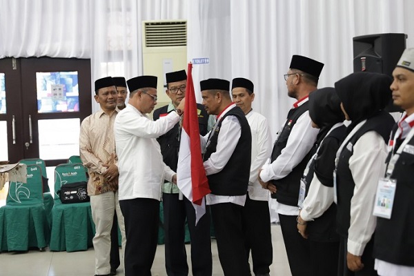 Sekda Pidie H.Idhami, S.Sos, MSi menyerahkan Bendera Merah Putih kepada petugas kloter 02 di Aula Jeddah Asrama Haji Aceh, Rabu (24/05/23) malam. (Waspada/T.Mansursyah)