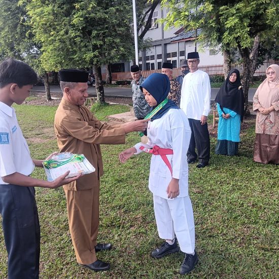 Kepala SMP Negeri 2 Langsa Drs Abdul Mutaleb menyematkan medali penghargaan kepada seorang siswi yang berprestasi Naura Letisya. (Waspada/Ibnu Sa'dan).