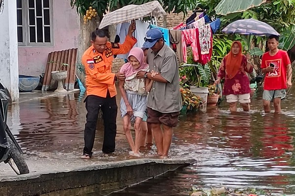 Personel BPBD Muhammad Rudi sedang membantu Lansia saat melintasi banjir di Kec Simpangempat, Kab Asahan. Waspada/Sapriadi