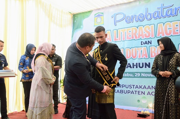 Pj Bupati Aceh Besar, Muhammad Iswanto, memasang selempang kepada Safrizal sebagai Duta Baca Aceh Besar Tahun 2023 di Halaman Dinas Perpustakaan dan Kearsipan Aceh Besar, Kota Jantho, Rabu (29/11). (Waspada/Zafrullah)