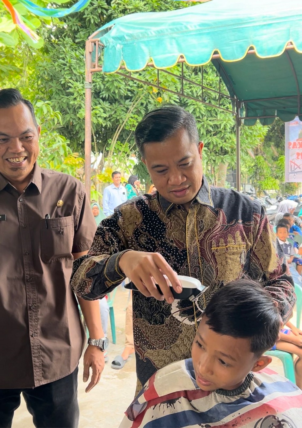 Pj Wali Kota Tebingtinggi, Dr Moettaqien Hasrimi, S.STP, M.Si didampingi Camat Rambutan, Marwansyah Harahap saat memangkas rambut remaja yang hadir pada kegiatan pangkas gratis di Kantor Kecamatan Rambutan, Kota Tebingtinggi. Waspada/Kristian Brahmana
