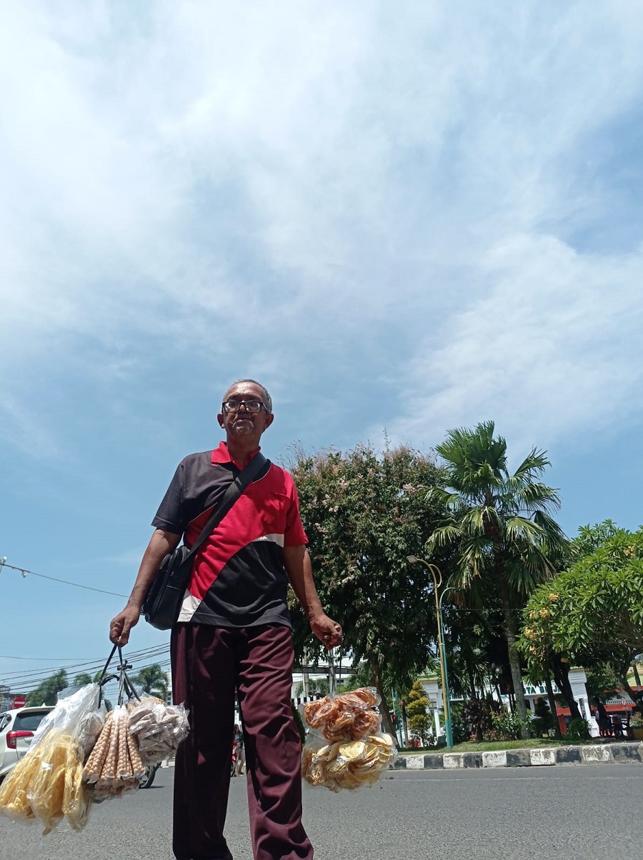 Seorang pedagang jajanan keliling berjalan kaki di bawah terik panas matahari di Jalan Veteran, Binjai Kota. (Waspada/Ria Hamdani)